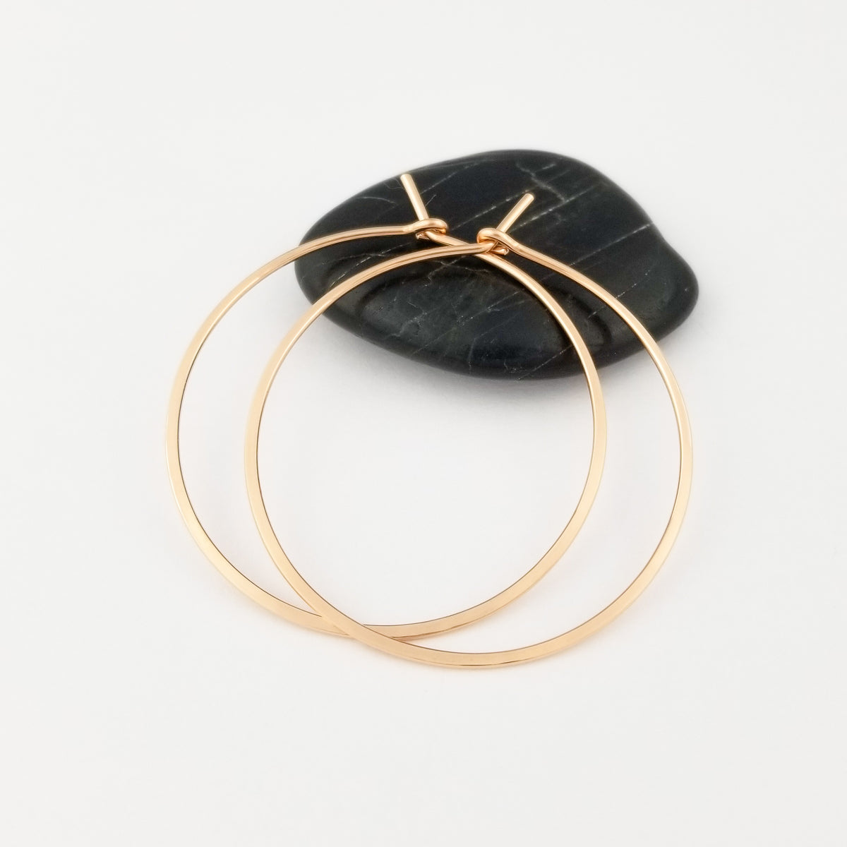 Solid 14k Rose Gold Flat Hammered Classic Hoop Earrings on a Black Rock