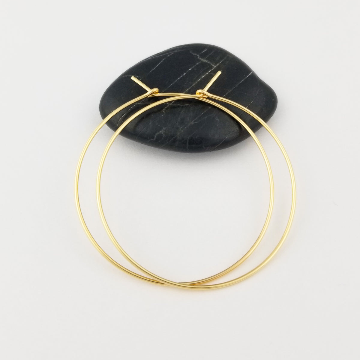 Solid Gold Hoop Earrings made with Thin Solid Yellow Gold 14 Karat Metal Wire on Black Rock