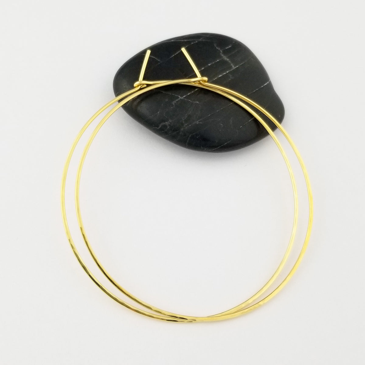 Thin Solid Yellow Gold Hammered Hoop Earrings Sitting on Black Rock